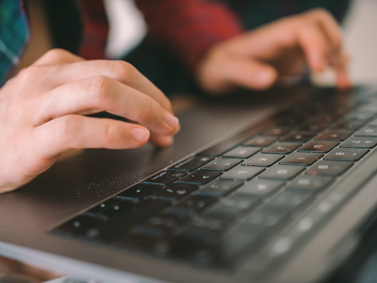 Tangan mengetik di laptop saat menyusun artikel